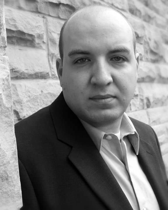 A grayscale image of Dr. Matthew Tozer standing in front of a stone wall